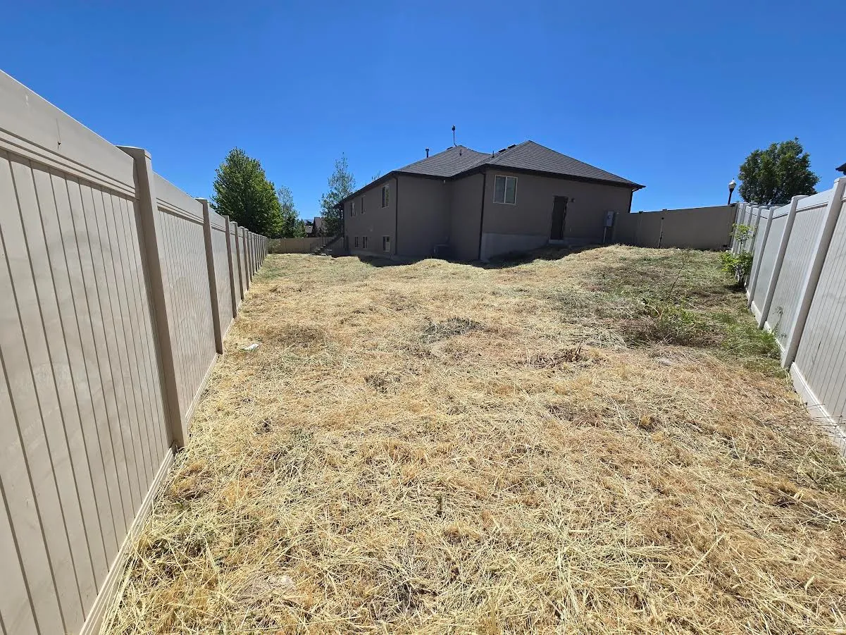 Expansive rear yard featuring a tan privacy fence and a two-story residence with a dark roofline