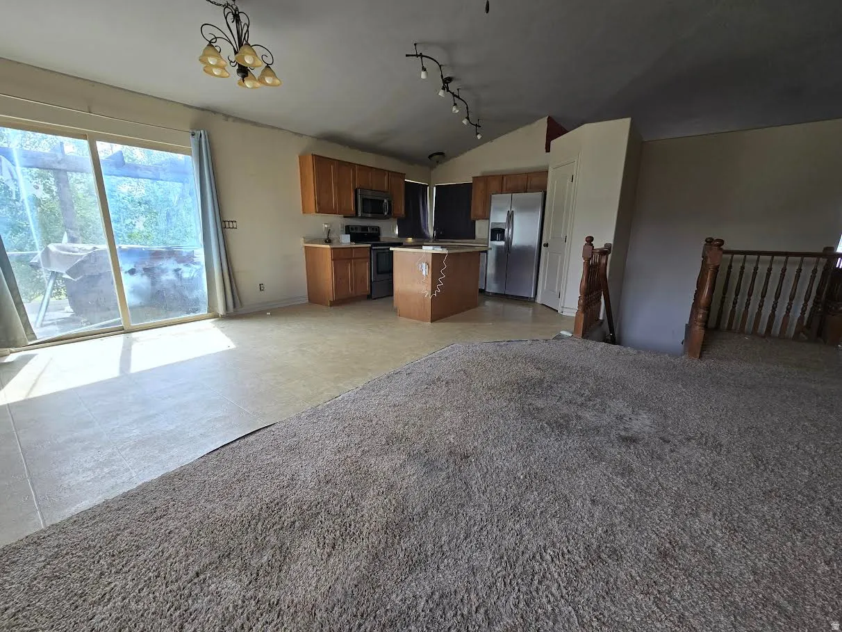 Open-concept kitchen and living area featuring a sliding glass door, a kitchen island, wood cabinetry, stainless steel appliances, and a staircase with wood railings