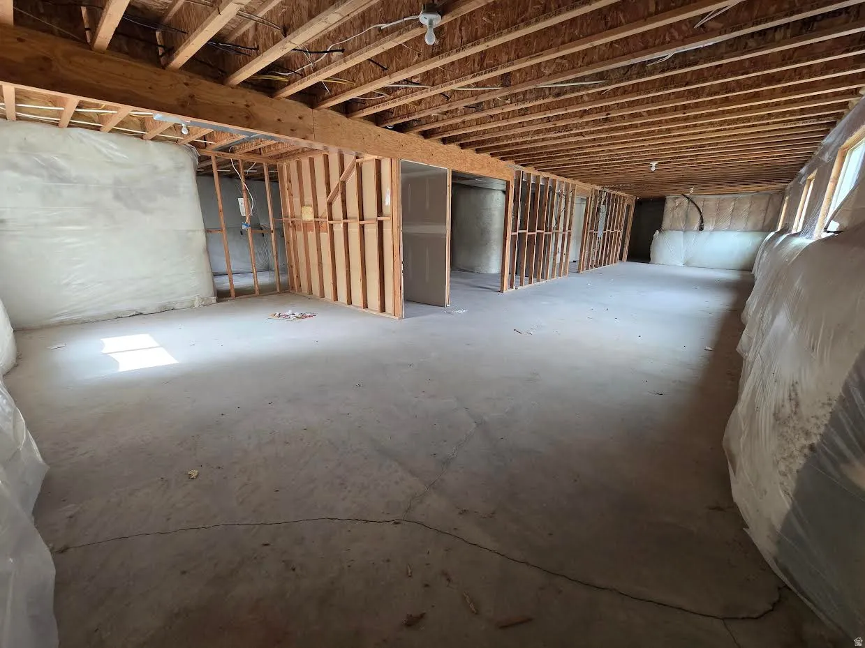 Spacious unfinished basement featuring exposed ceiling joists, framed interior walls, concrete flooring, and multiple window openings with insulation