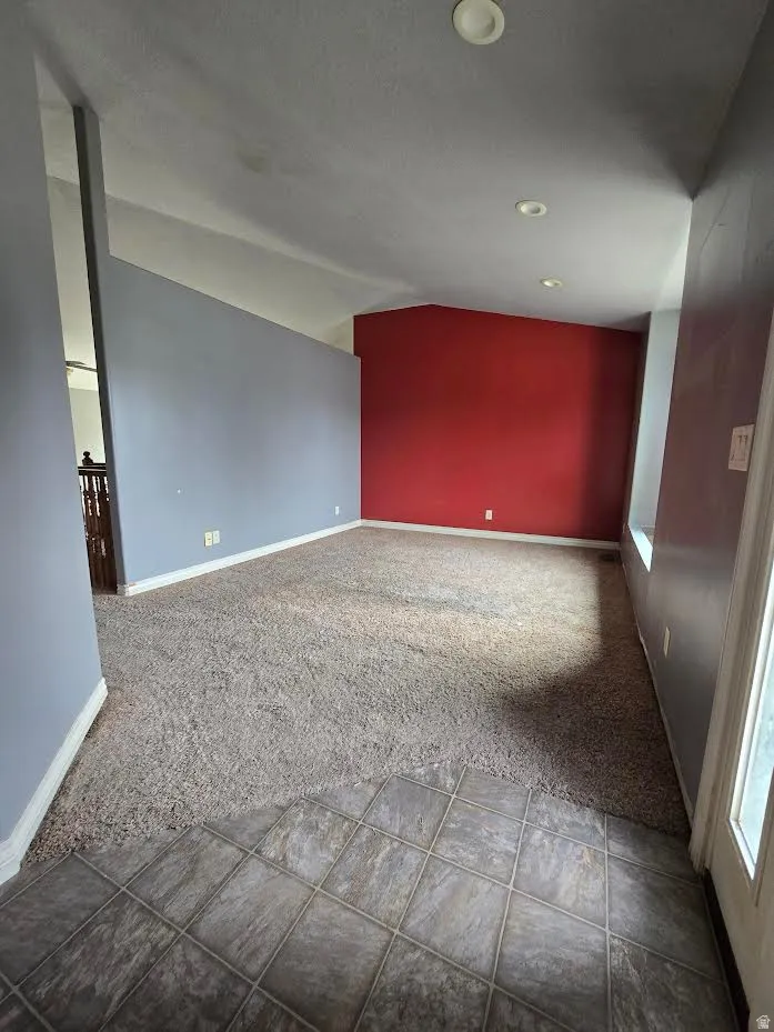 Spacious room featuring vaulted ceilings, recessed lighting, and a combination of carpet and tiled flooring