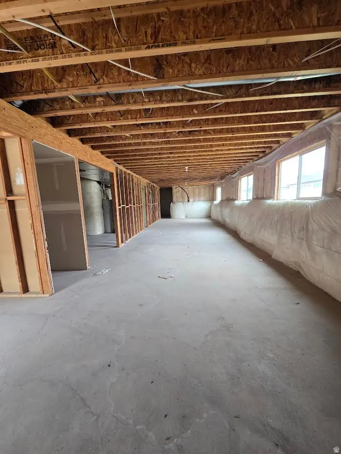 Unfinished basement featuring exposed wood joists, framed interior walls, concrete flooring, and windows providing natural light