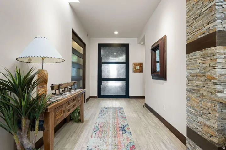 Entryway featuring a stacked stone accent wall with wood beam details, light wood-finish flooring, and a modern black entry door with frosted glass panels