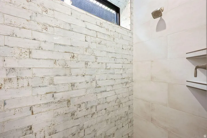 Shower featuring a distressed white brick-style wall, large format tile, a bronze-finish showerhead, and a built-in shelving niche with bronze-finish fixtures