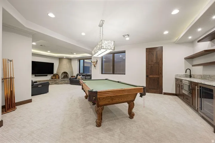 Spacious recreational room featuring a stone fireplace, recessed lighting, and a wet bar with granite countertops