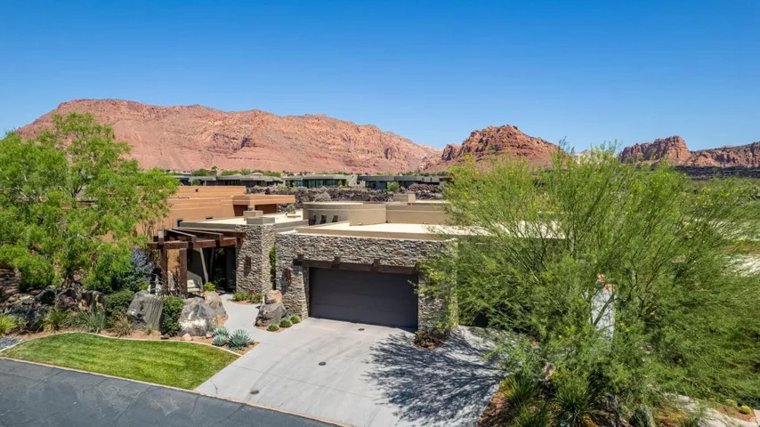 Modern desert-style residence with a stone facade, integrated garage, and a lush, rock-accented landscape