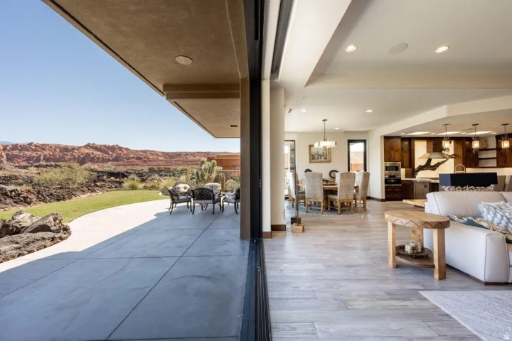 Expansive sliding glass doors opening to a concrete patio, a manicured lawn, and distant natural rock formations