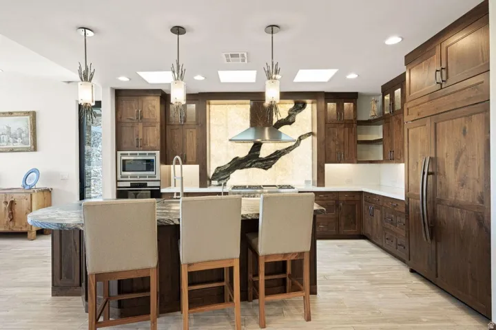 Kitchen featuring dark wood cabinetry, a large center island with seating, integrated panel-front refrigerator, stainless steel appliances, and multiple skylights