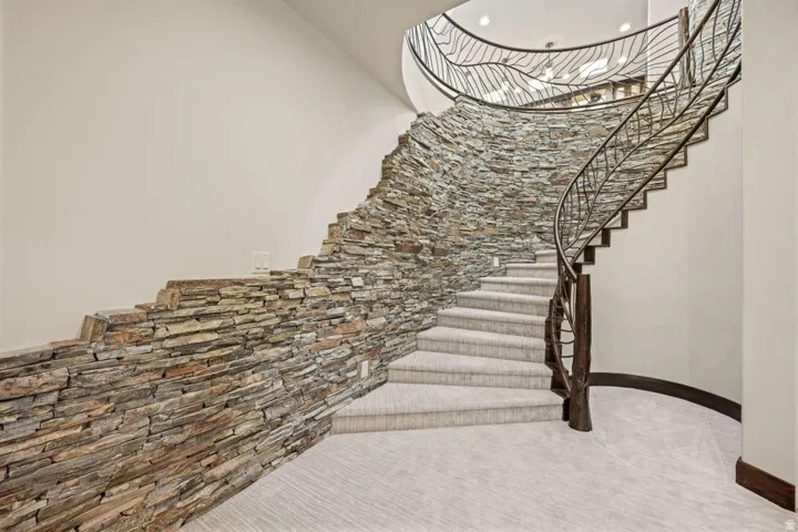 Curved staircase featuring a stone accent wall, wrought iron railing, wood newel post, and light-colored carpeted treads
