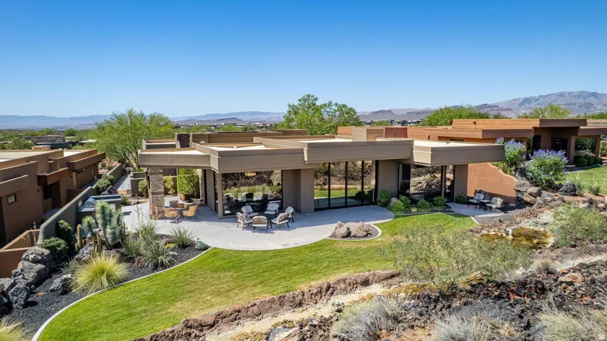 Contemporary desert architecture featuring expansive floor-to-ceiling windows, a spacious patio area, and a manicured lawn