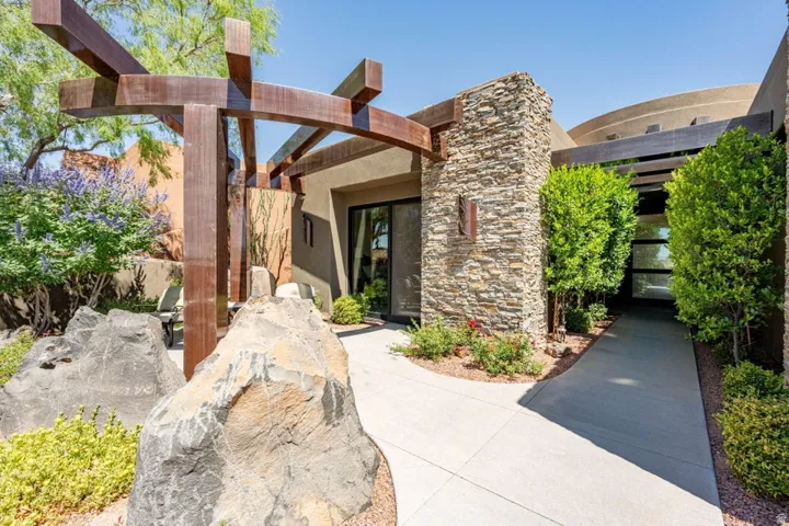 Exterior entry featuring a paved walkway, stone-clad walls, and a wooden pergola structure