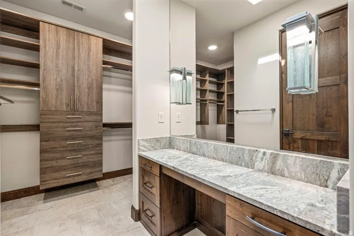 Dressing area featuring a vanity with a large mirror, stone countertop, built-in storage, and integrated shelving