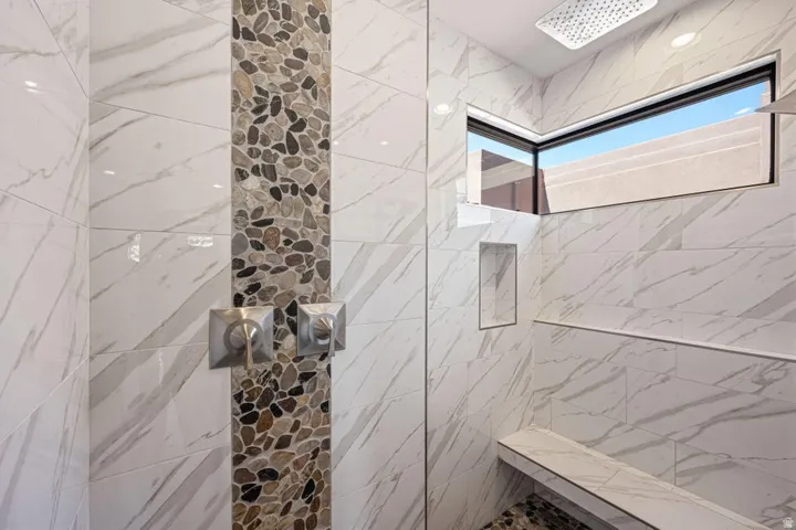 Walk-in shower with natural stone pebble accent tile, large format marble-look wall tile, a built-in bench, and a rectangular transom window