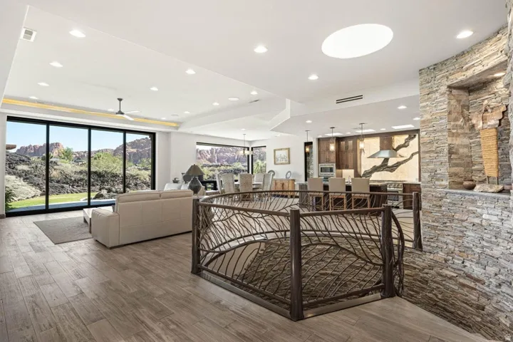 Open concept living space featuring a custom metal railing, stone accent wall, large format wood-finish flooring, recessed lighting, and expansive glass sliding doors