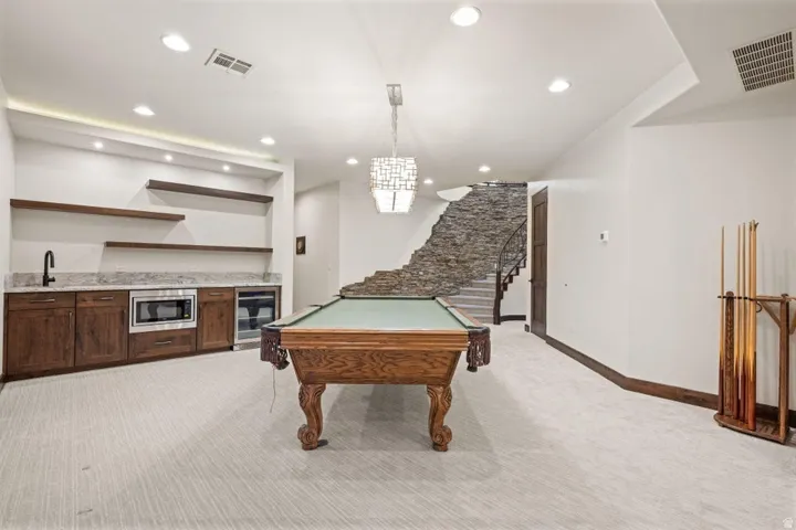 Spacious entertainment area featuring a stone-clad staircase, built-in wet bar with wood cabinetry, integrated microwave, and beverage cooler