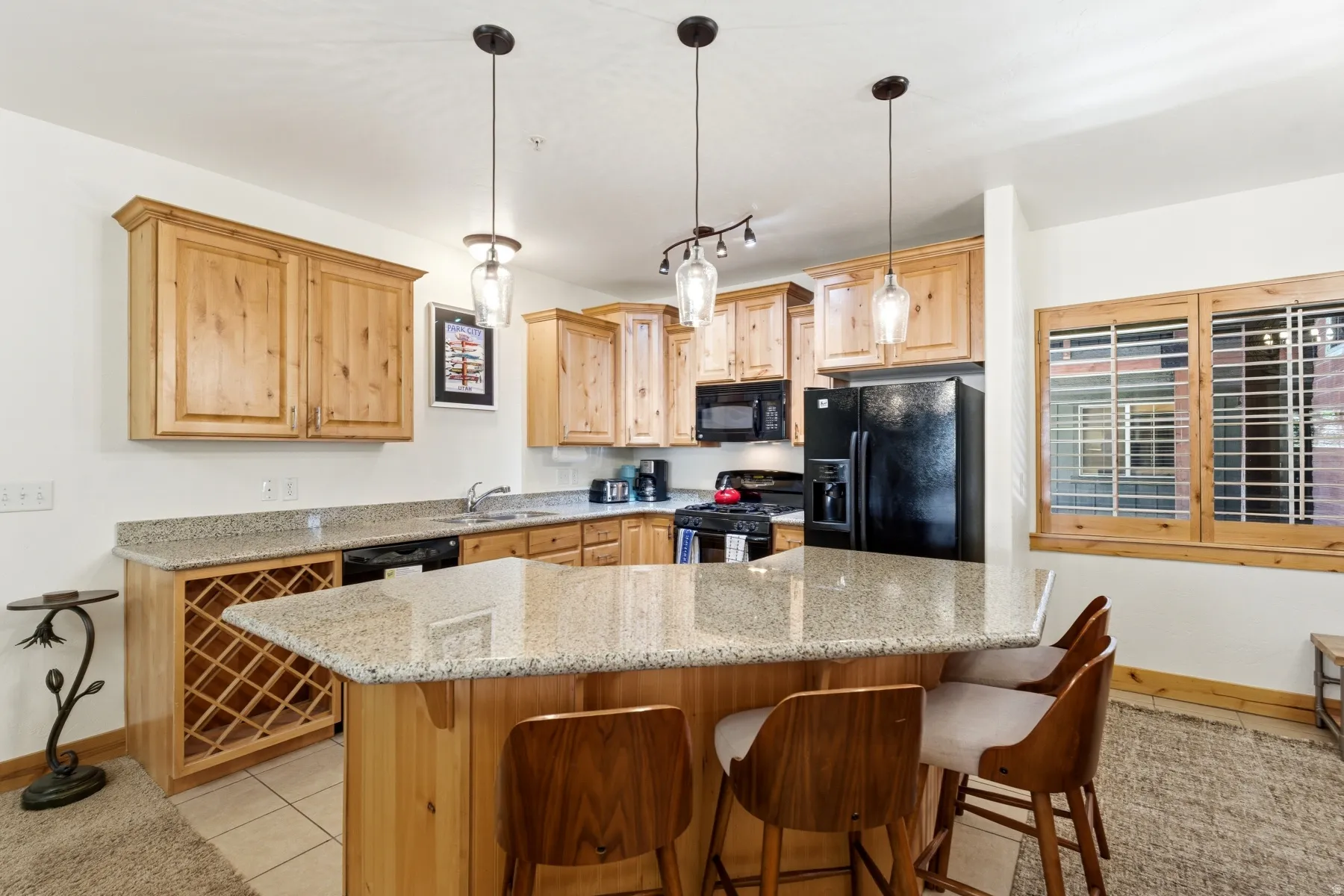 Kitchen featuring light wood cabinetry, granite-style countertops, black appliances, and a built-in wine rack