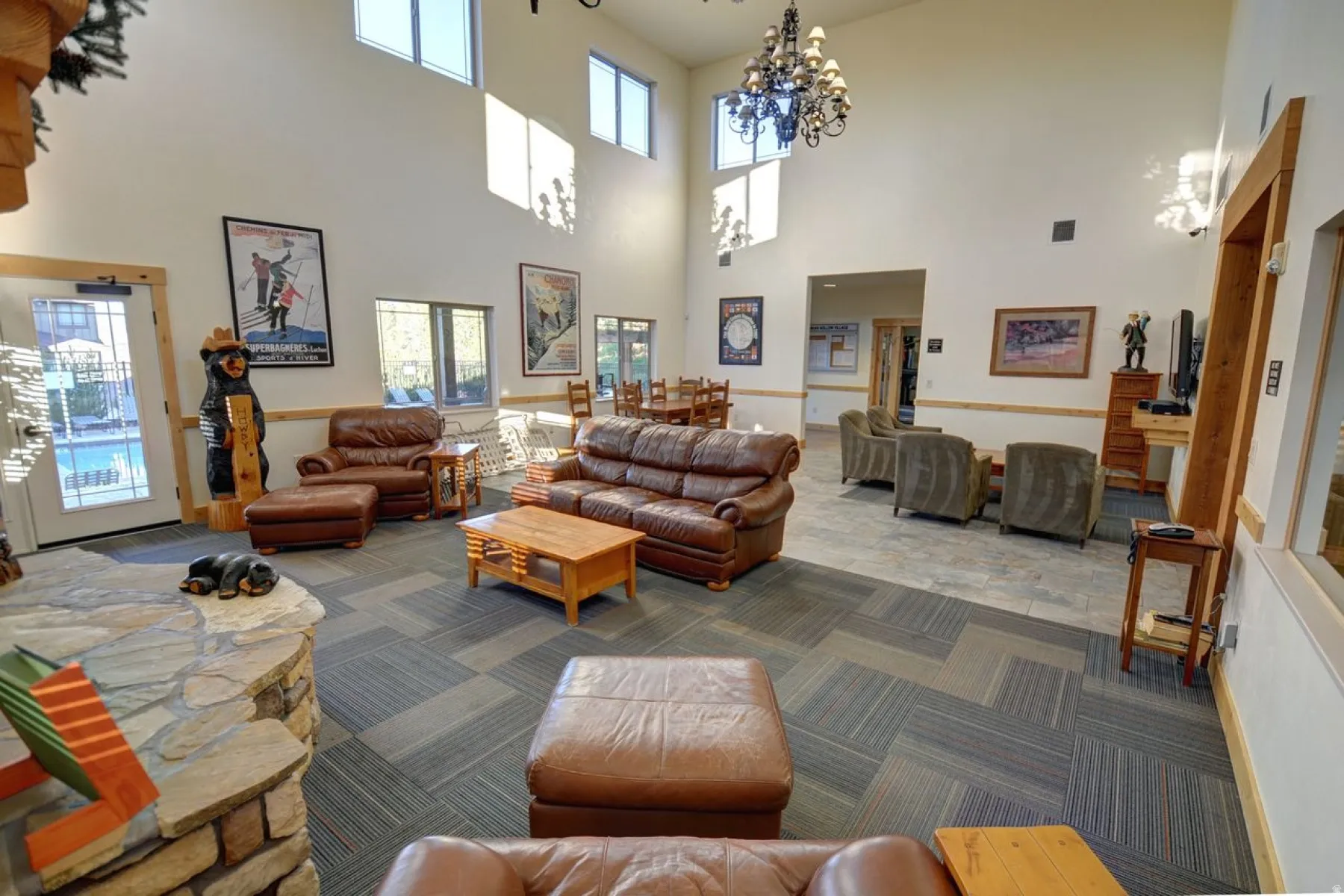 Spacious common area featuring a stone fireplace, high ceilings, large windows, and patterned carpet flooring
