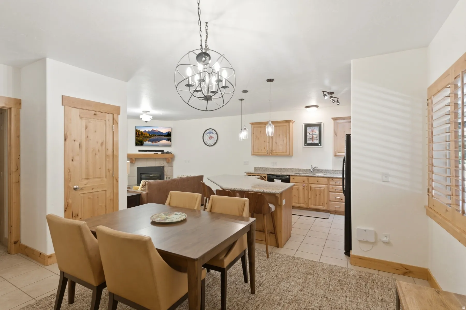 Open-concept living area featuring a dining space with a decorative chandelier, a kitchen with light wood cabinetry and a breakfast bar, and a living room with a fireplace