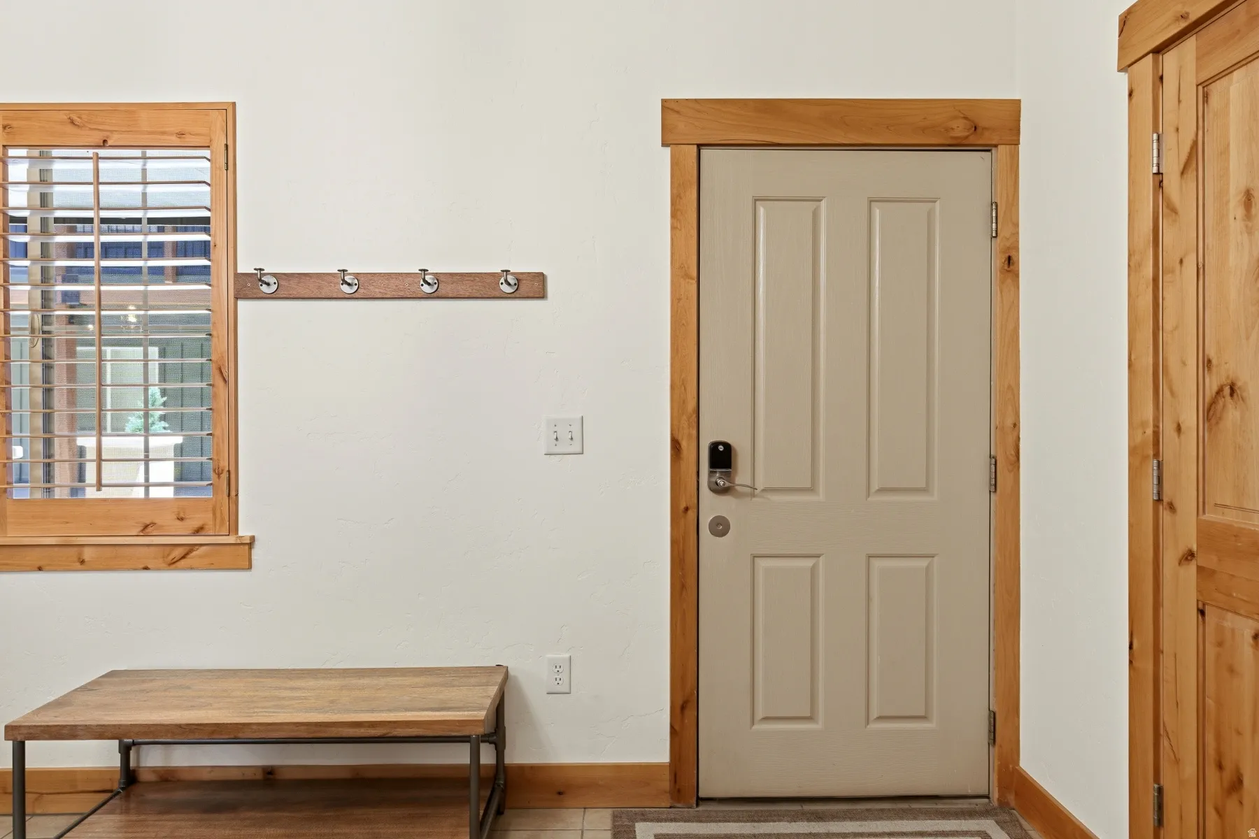 Entryway featuring a panel door with smart lock hardware, natural wood trim, and a window with plantation shutters