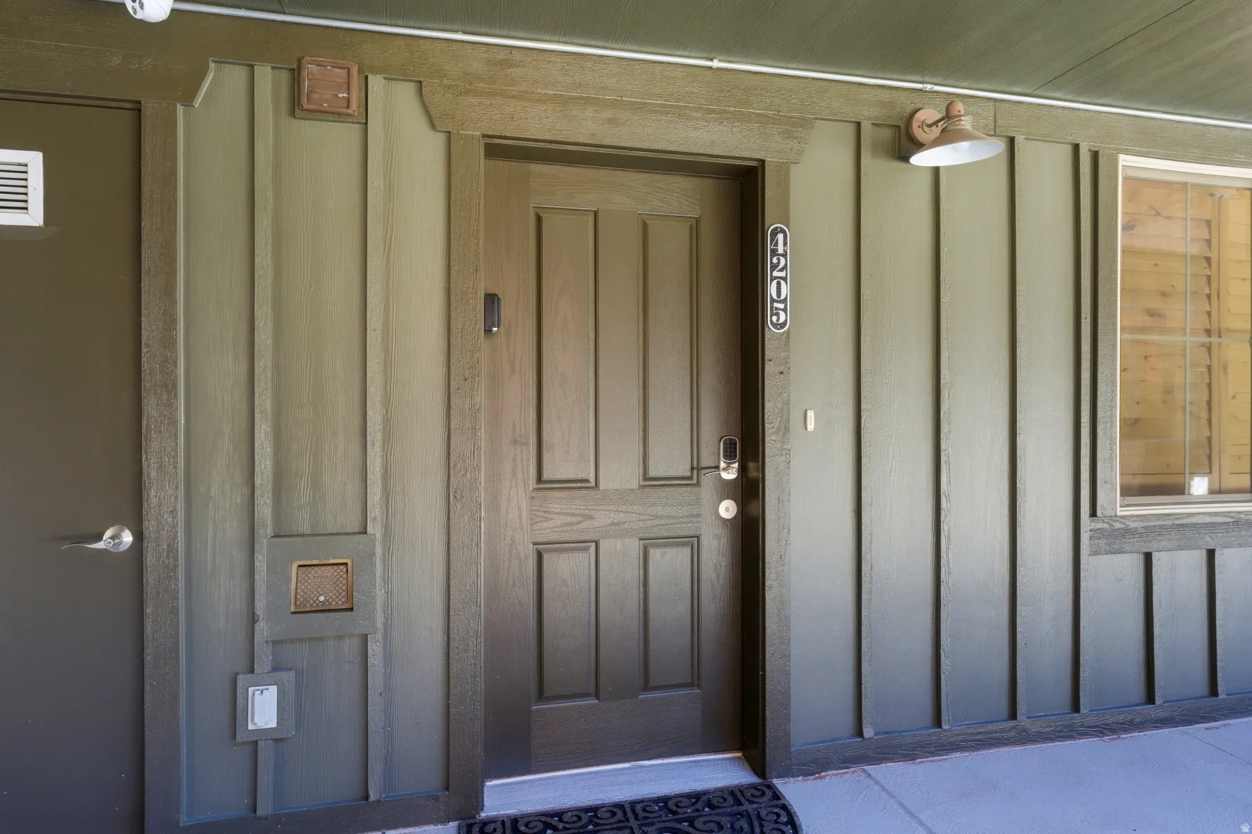 Panel siding exterior in a neutral green tone featuring a prominent entry door