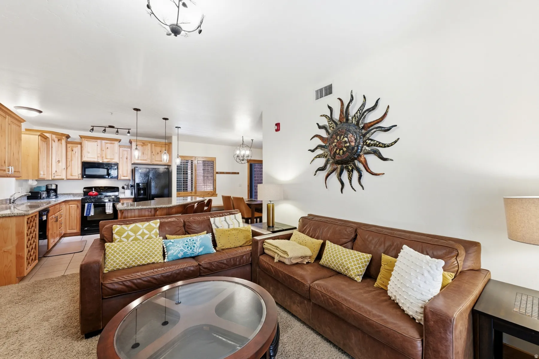 Open-concept living area featuring a kitchen with light wood cabinetry, stone-finish countertops, and black appliances