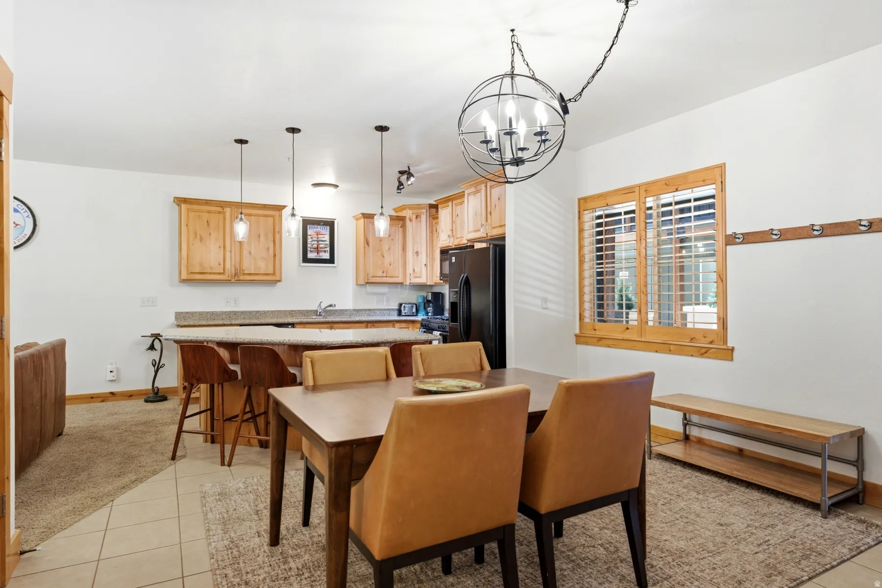 Open-concept dining and kitchen area featuring natural wood cabinetry, a breakfast bar with seating, pendant lighting, and a large window with plantation shutters