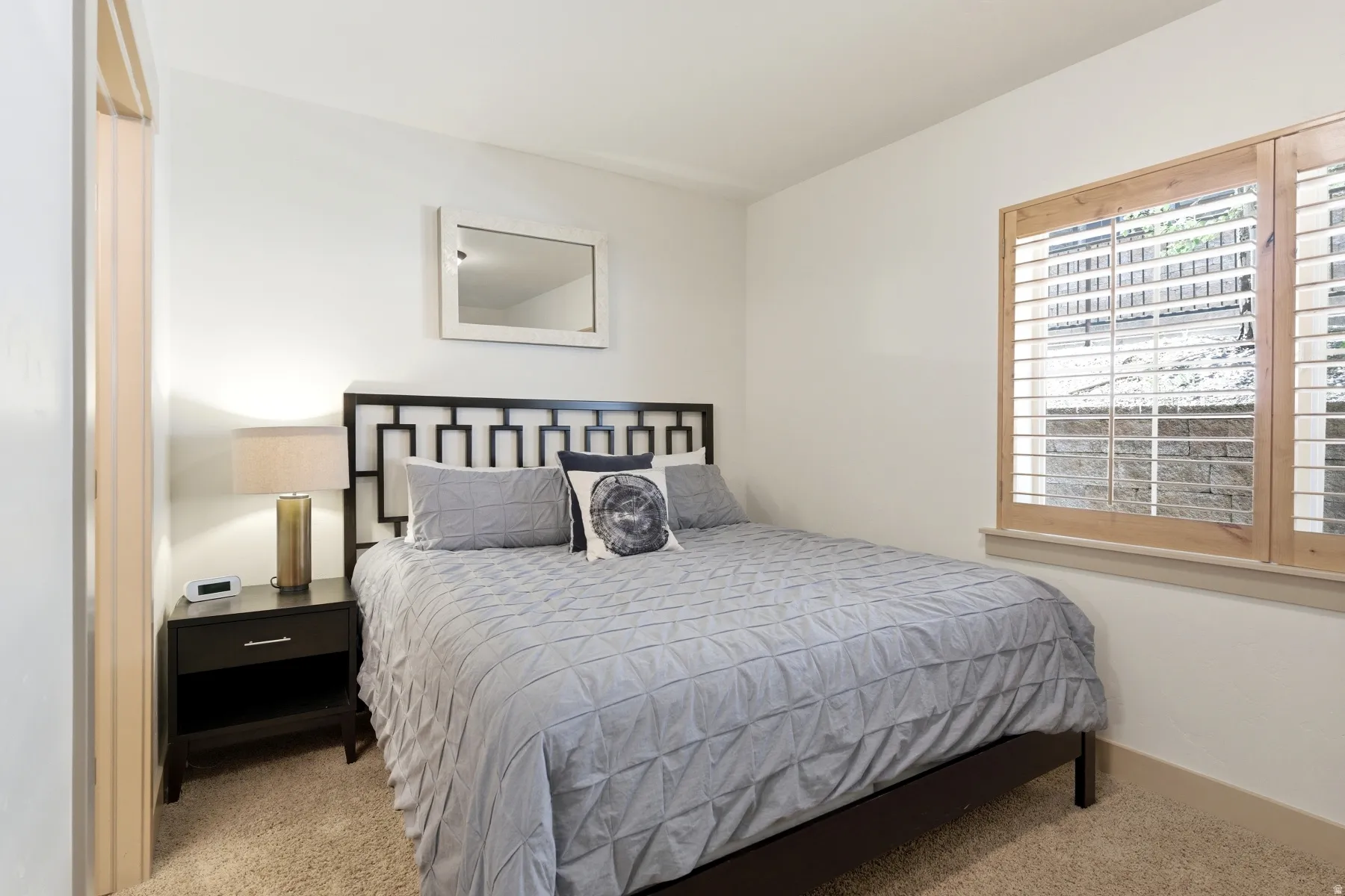 Carpeted room featuring a window with wood-frame plantation shutters, a dark wood geometric headboard, and a built-in dark wood nightstand
