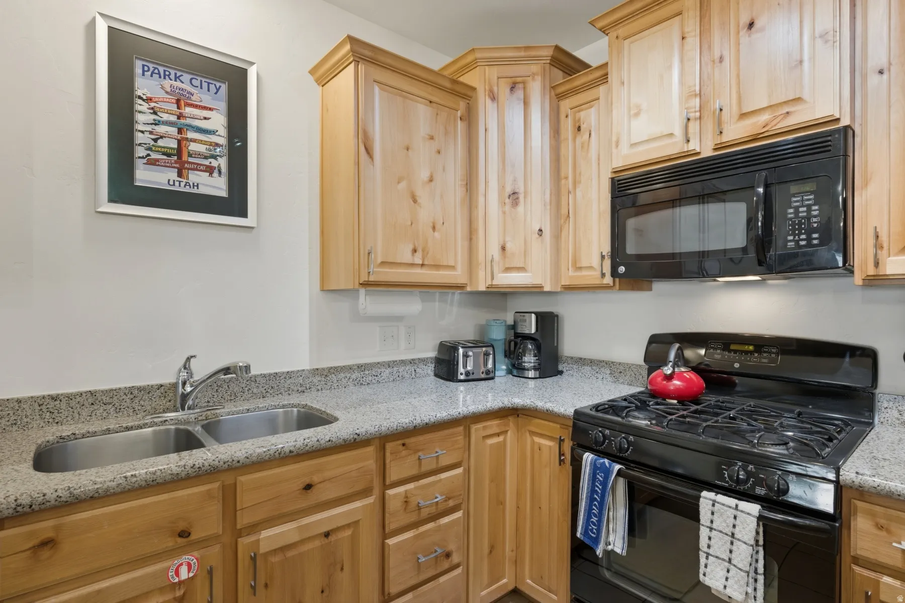 Kitchen featuring wood-finish cabinetry, speckled countertops, a double basin stainless steel sink, a black gas range, and a black built-in microwave