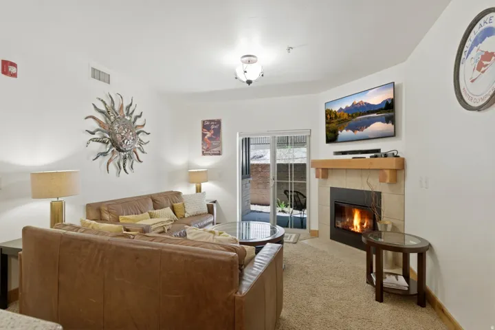 Living area featuring a gas fireplace with a tiled surround and wood mantle, wall-mounted television, and sliding glass door access to an exterior patio