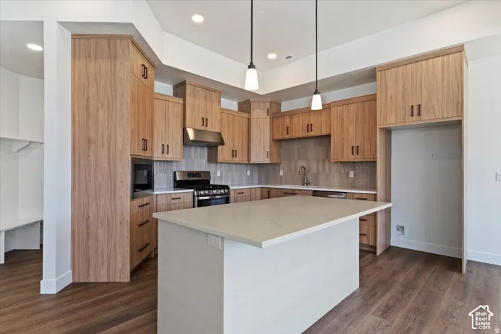Modern kitchen featuring wood-finish cabinetry, a large center island with a light-toned countertop, stainless steel appliances, and pendant lighting