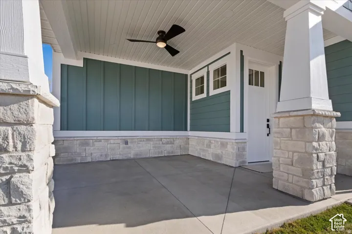 Covered front porch featuring a ceiling fan, stone-clad columns, horizontal siding, and a white entry door with upper window panes