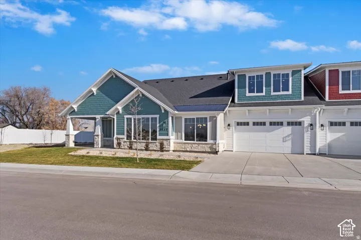 Modern facade featuring teal horizontal siding and shaker shingles, stone accents, a covered entry, and a two-car garage with transom windows