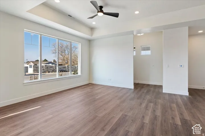 Spacious room featuring wood-finish flooring, a large multi-pane window, and a tray ceiling with recessed lighting