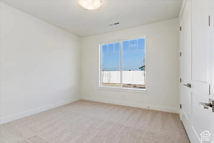 Neutral color palette room featuring a large window, light-toned carpet, white baseboards, and white paneled doors with brushed nickel hardware