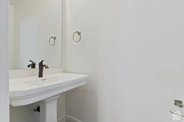 Pedestal sink with a dark bronze faucet, accompanied by a frameless wall-mounted mirror