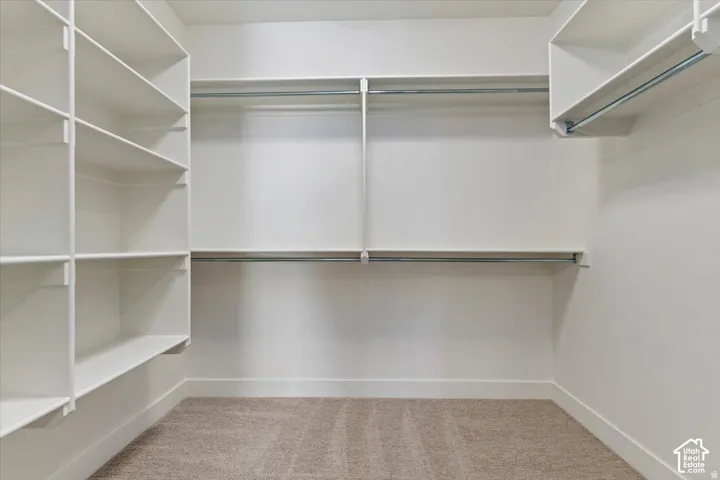 Walk-in closet featuring white built-in shelving, multiple hanging rods, and neutral-toned carpeting