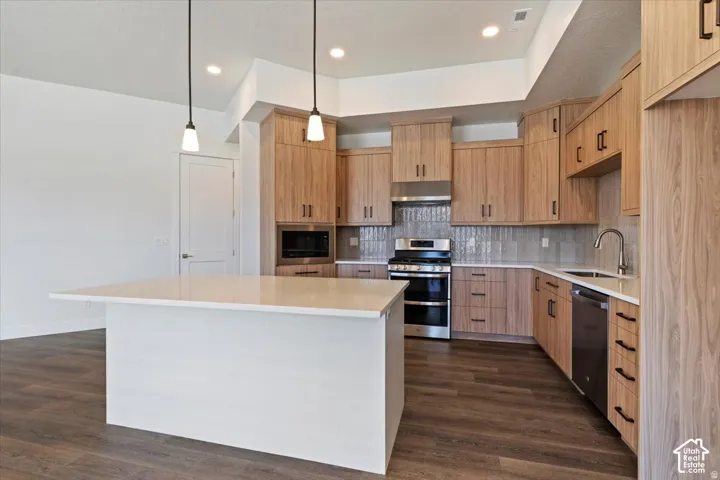 Modern kitchen featuring a large white island with a solid surface countertop, light wood-finish cabinetry, stainless steel appliances, a tiled backsplash, and recessed lighting