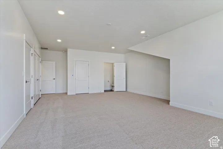 Spacious room featuring light-toned carpet, recessed lighting, white walls, multiple white panel doors, and substantial white baseboards
