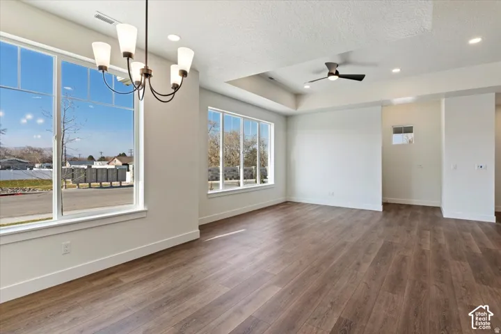 Spacious interior featuring large picture windows, wood-finish flooring, a tray ceiling with recessed lighting, a ceiling fan, and a contemporary chandelier