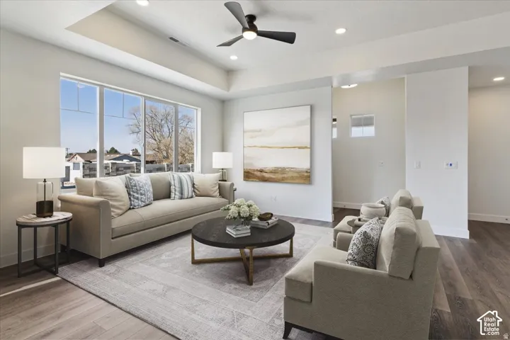 Spacious living area featuring large picture windows, a recessed tray ceiling, a contemporary ceiling fan, recessed lighting, and wood-finish flooring