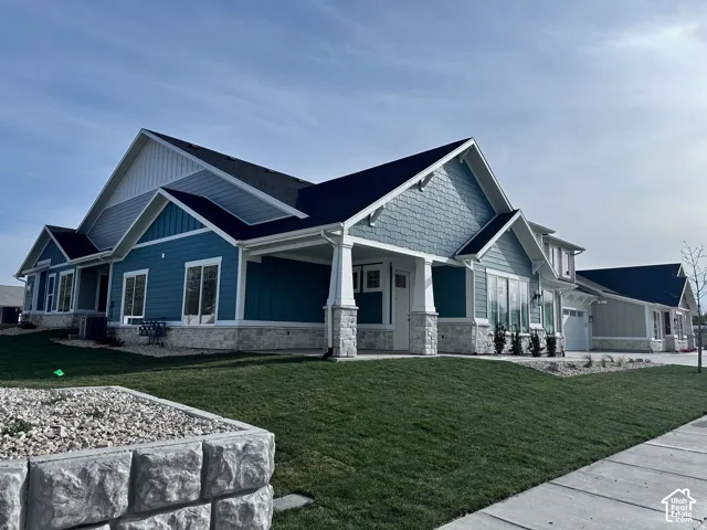 Modern ranch-style residence featuring blue siding, white trim, stone veneer accents, a covered front porch, and a well-maintained lawn