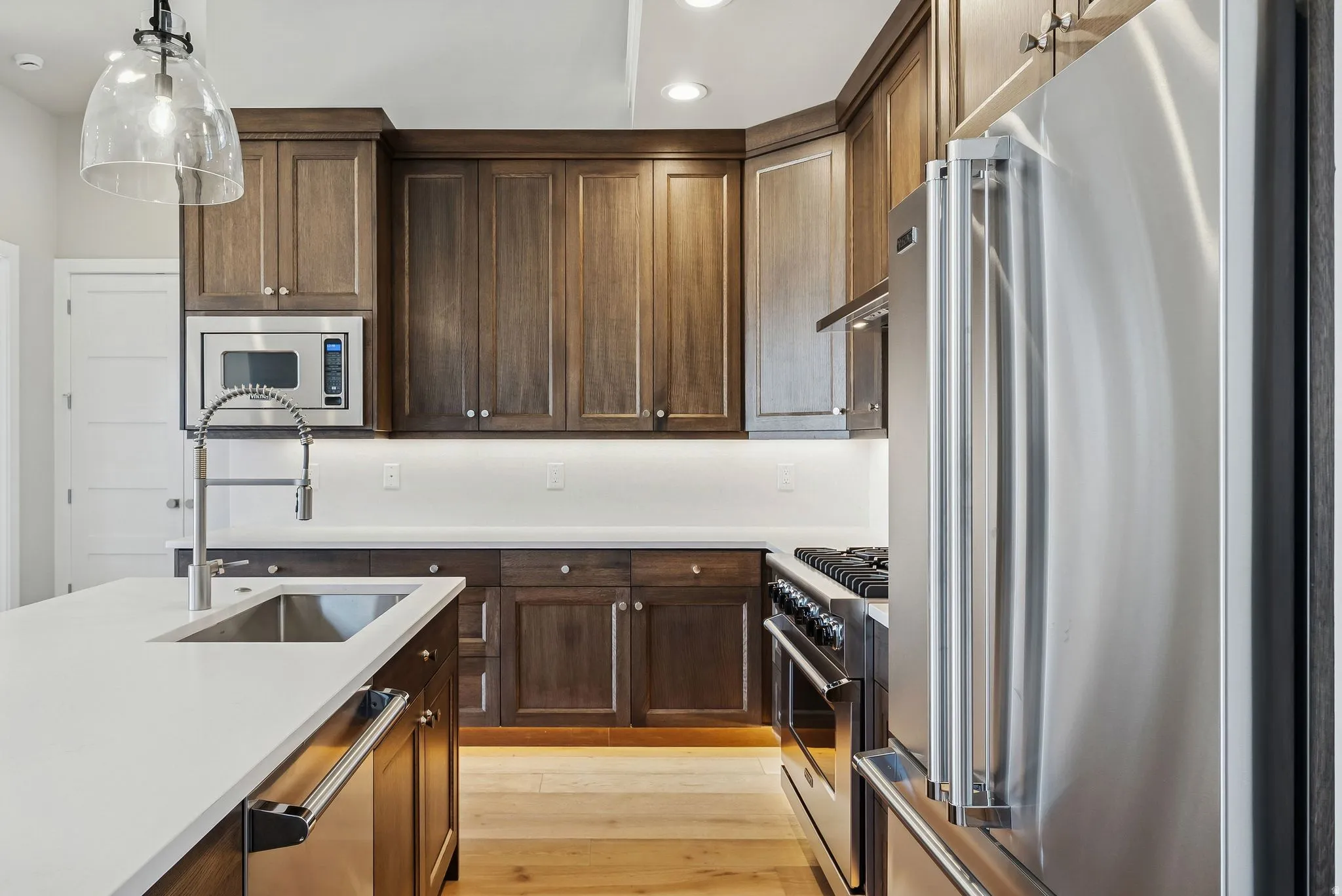 Gourmet kitchen featuring dark wood cabinetry, stainless steel appliances, white countertops, a large island with an undermount sink, and wood-finish flooring