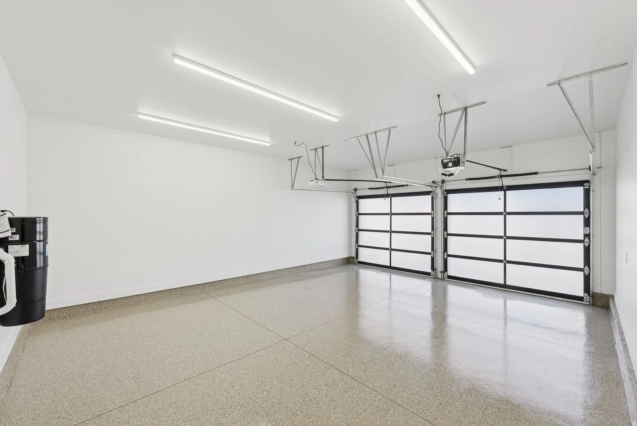 Spacious two-car garage featuring a speckled epoxy floor coating, two contemporary glass panel garage doors, and ample overhead lighting