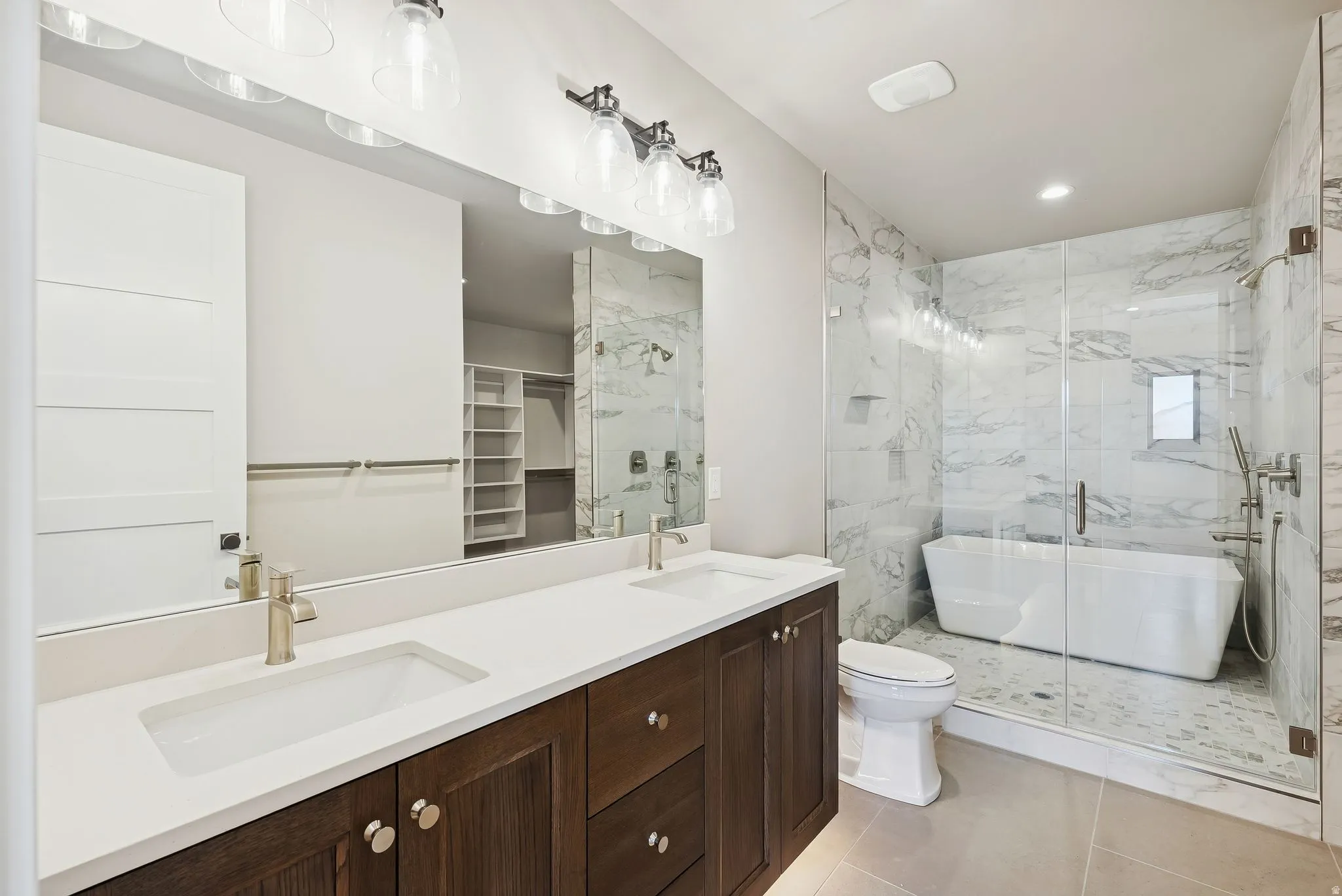Bathroom featuring a dual vanity with white countertops and dark wood cabinetry, a frameless glass shower enclosure, a freestanding soaking tub, and marble-look tile walls
