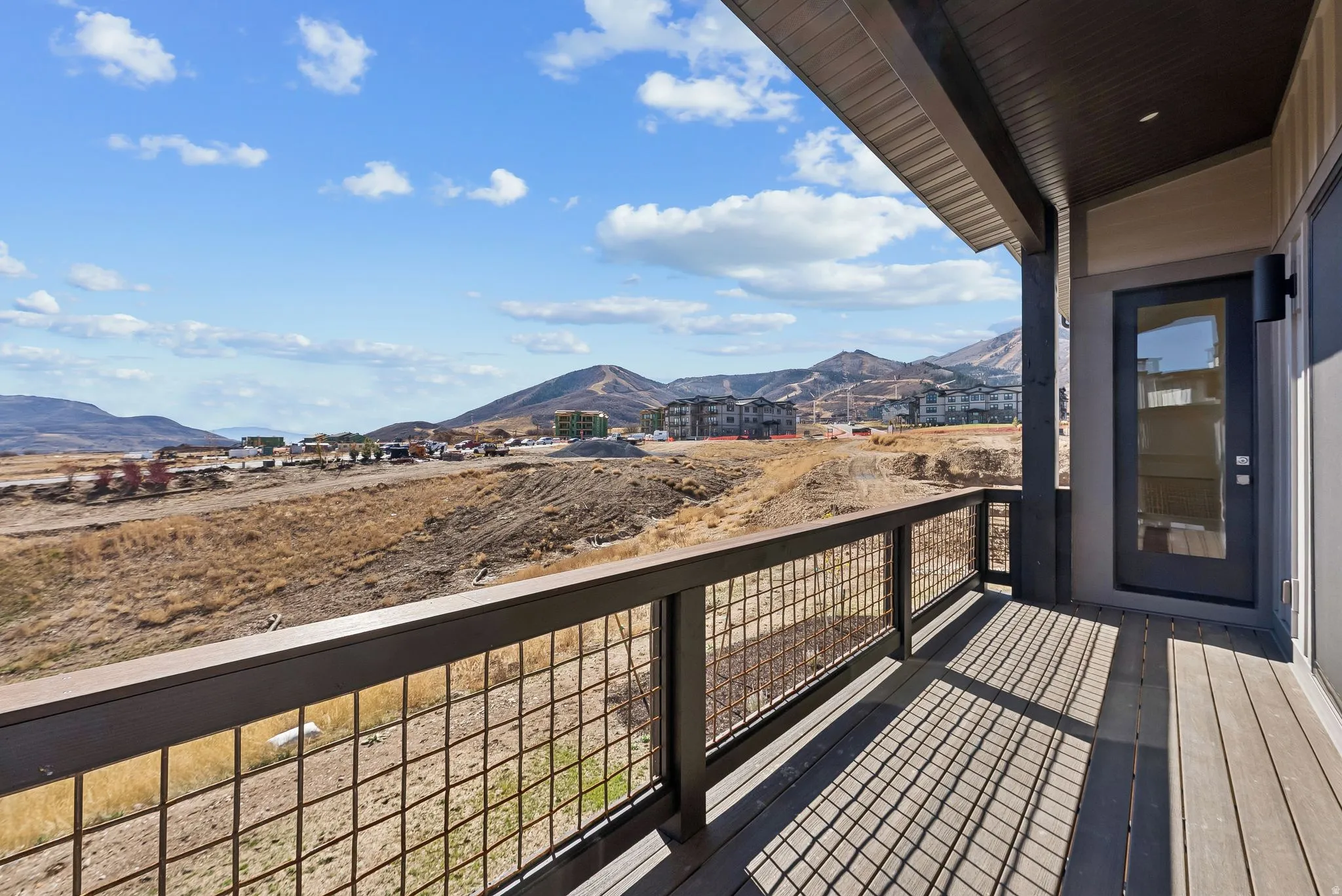 Spacious outdoor balcony featuring composite decking, a durable metal grid railing, and an exterior door with a full-light glass insert