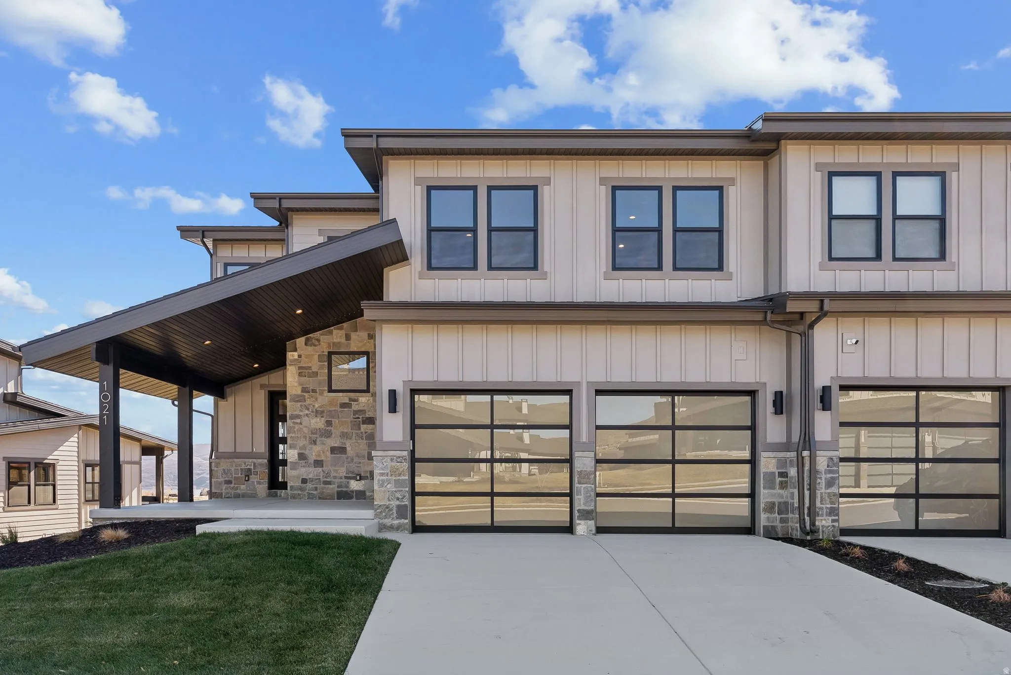 Modern multi-story exterior featuring a stone facade, vertical siding, and a prominent covered entryway with recessed lighting