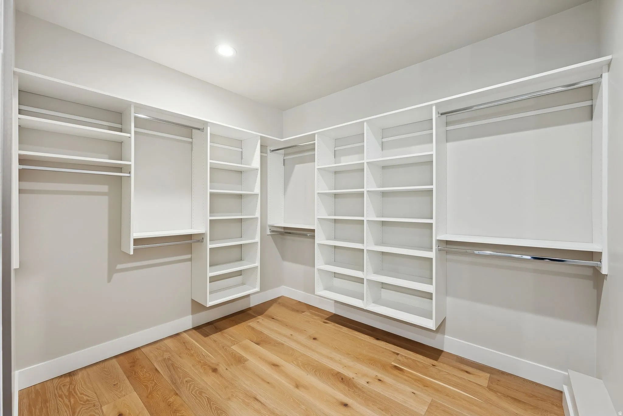 Spacious walk-in closet featuring extensive built-in shelving, multiple hanging rods, recessed ceiling lighting, and wood-finish flooring