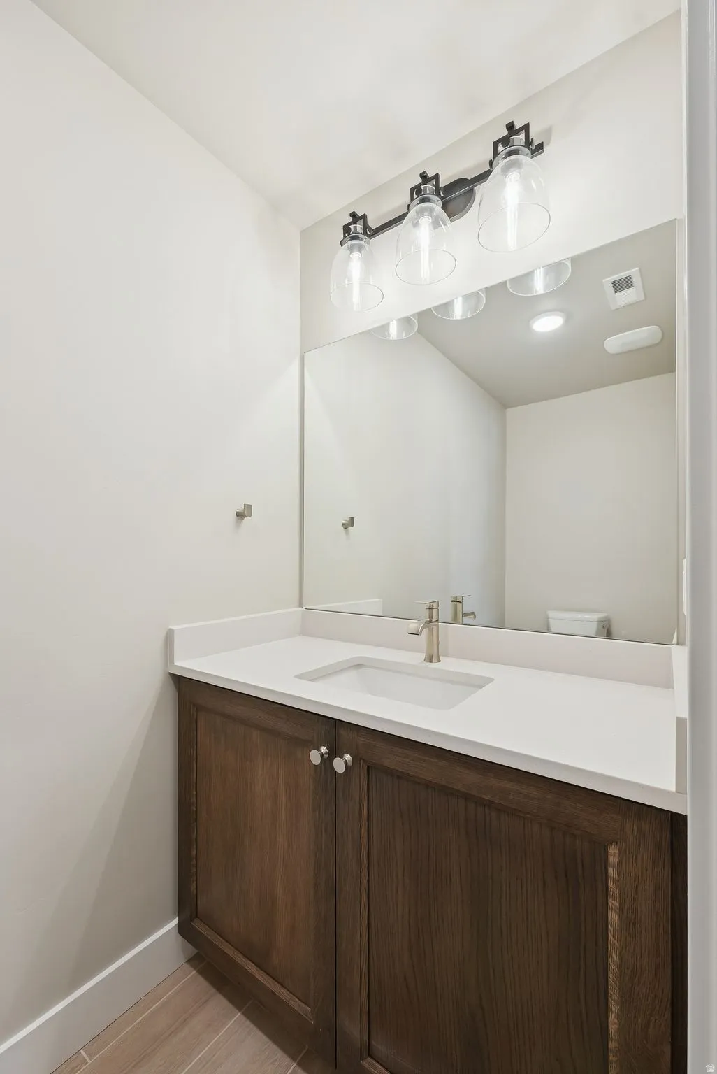 Vanity with wood-finish cabinetry, white countertop, and integrated sink