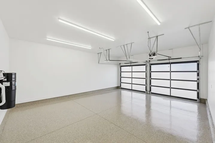 Spacious two-car garage featuring a speckled epoxy floor coating, two contemporary glass panel garage doors, and ample overhead lighting
