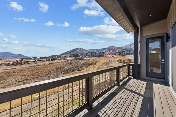 Spacious outdoor balcony featuring composite decking, a durable metal grid railing, and an exterior door with a full-light glass insert