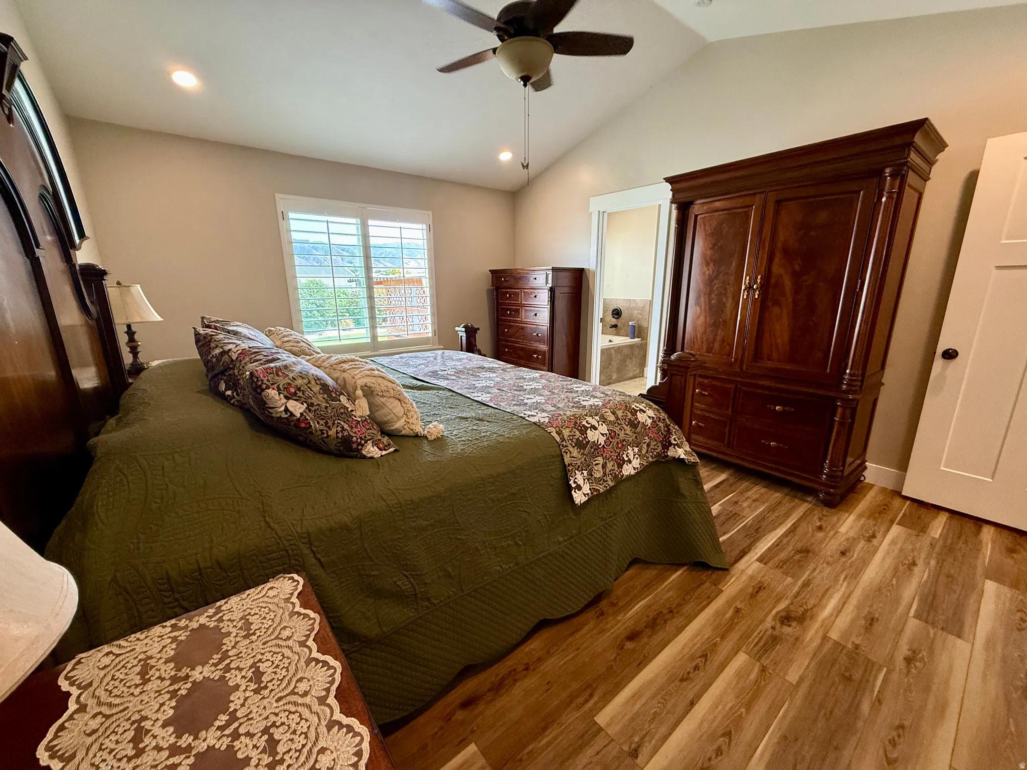 Spacious room featuring vaulted ceilings, wood-finish flooring, a ceiling fan with integrated lighting, recessed lighting, and a large window with white louvered shutters